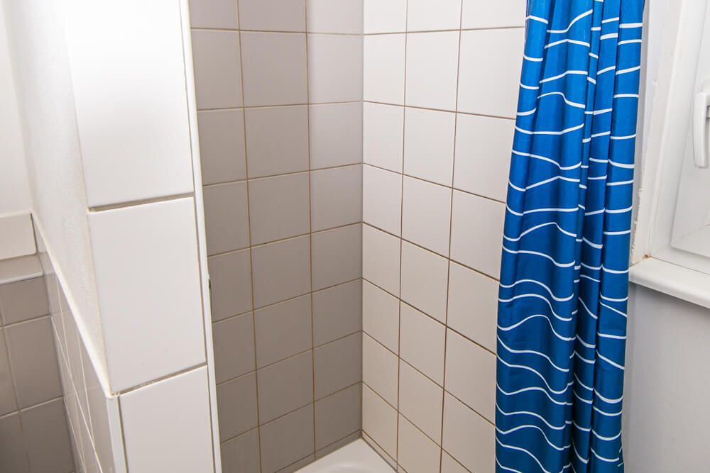Eckduschkabine mit blauem Vorhang im Badezimmer des Studentenwohnheims Solar